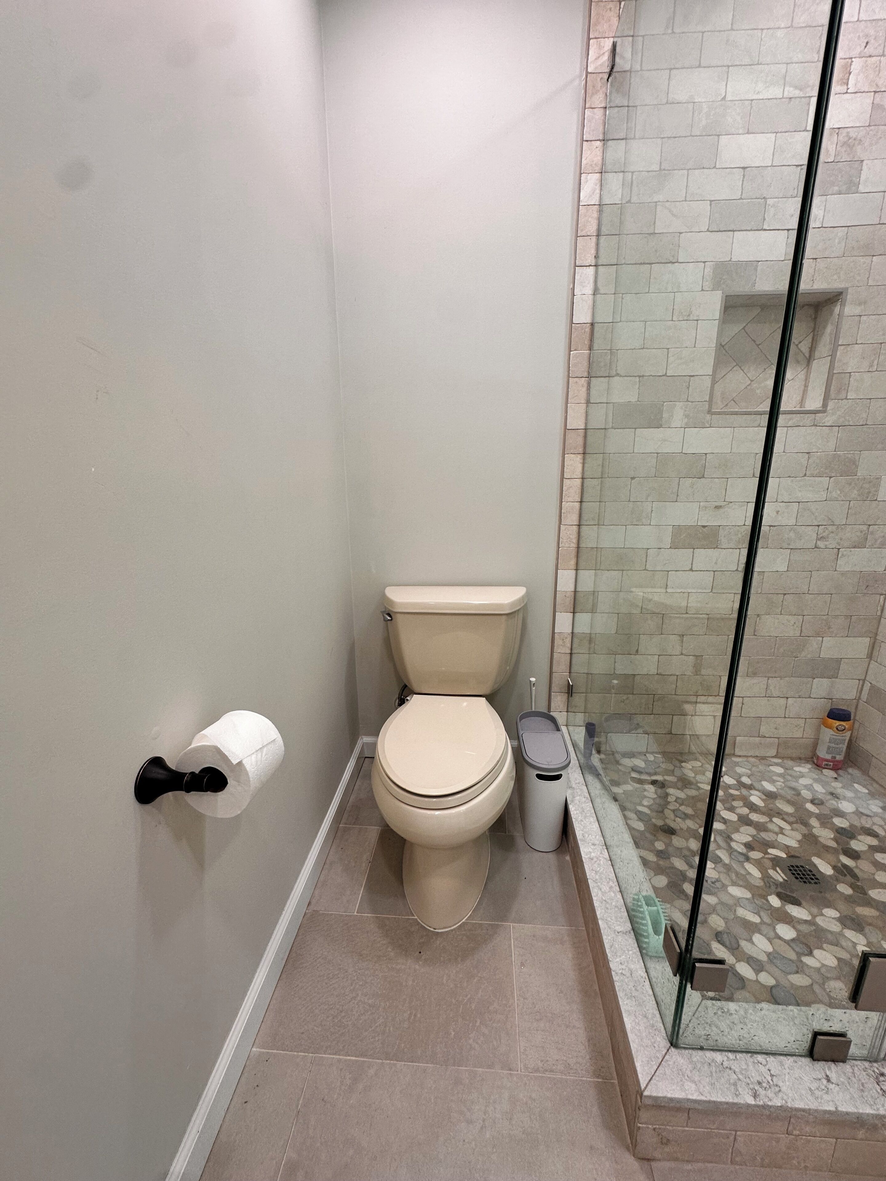 Kylpyhuone, jossa on wc, lasinen suihkuseinä ja roskakori.