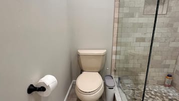 Kylpyhuone, jossa on wc, lasinen suihkuseinä ja roskakori.