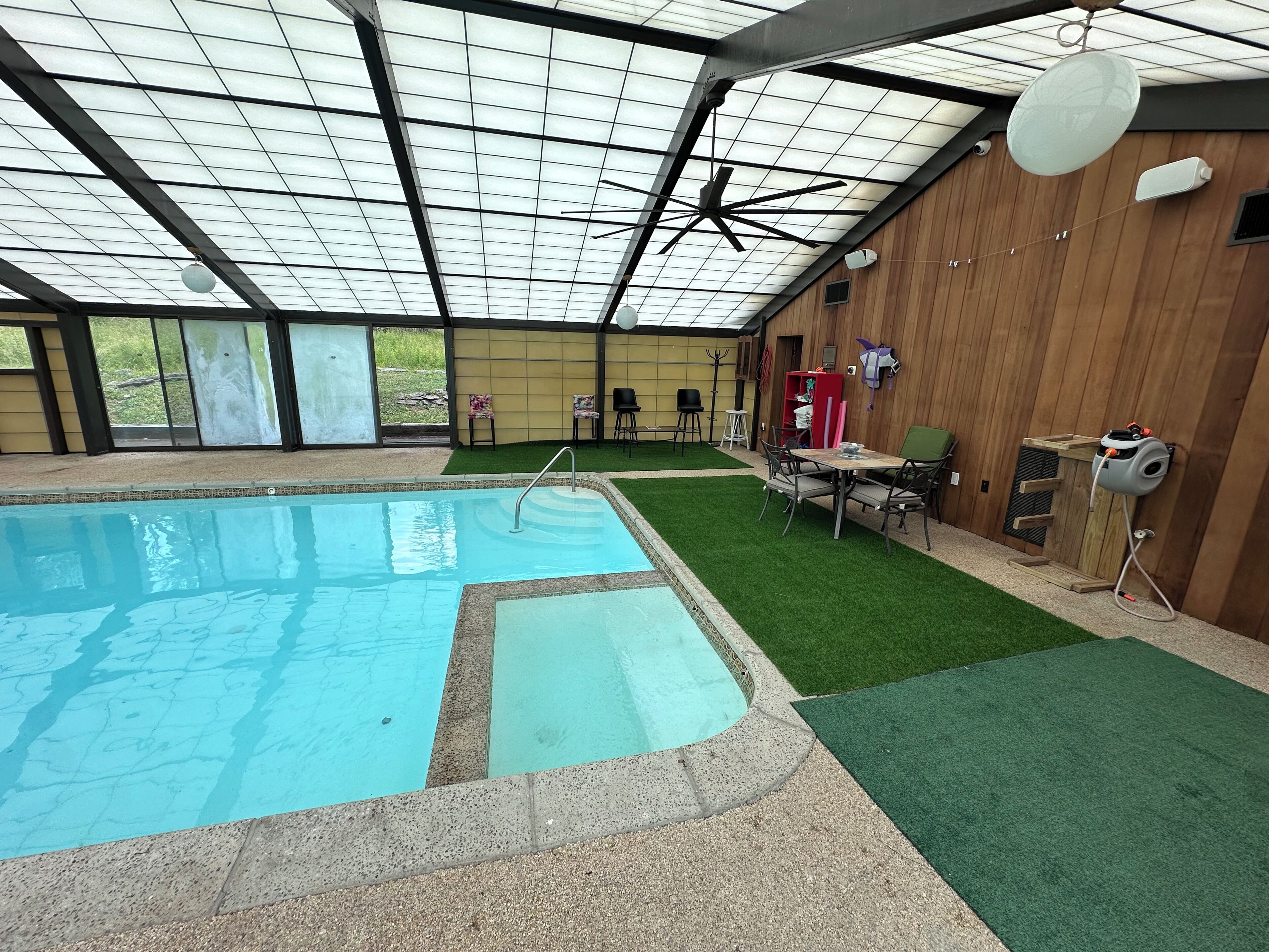 Une piscine intérieure dotée d’un ventilateur de plafond, d’un revêtement d’herbe artificielle et d’une table avec des chaises.