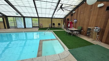 Une piscine intérieure dotée d’un ventilateur de plafond, d’un revêtement d’herbe artificielle et d’une table avec des chaises.