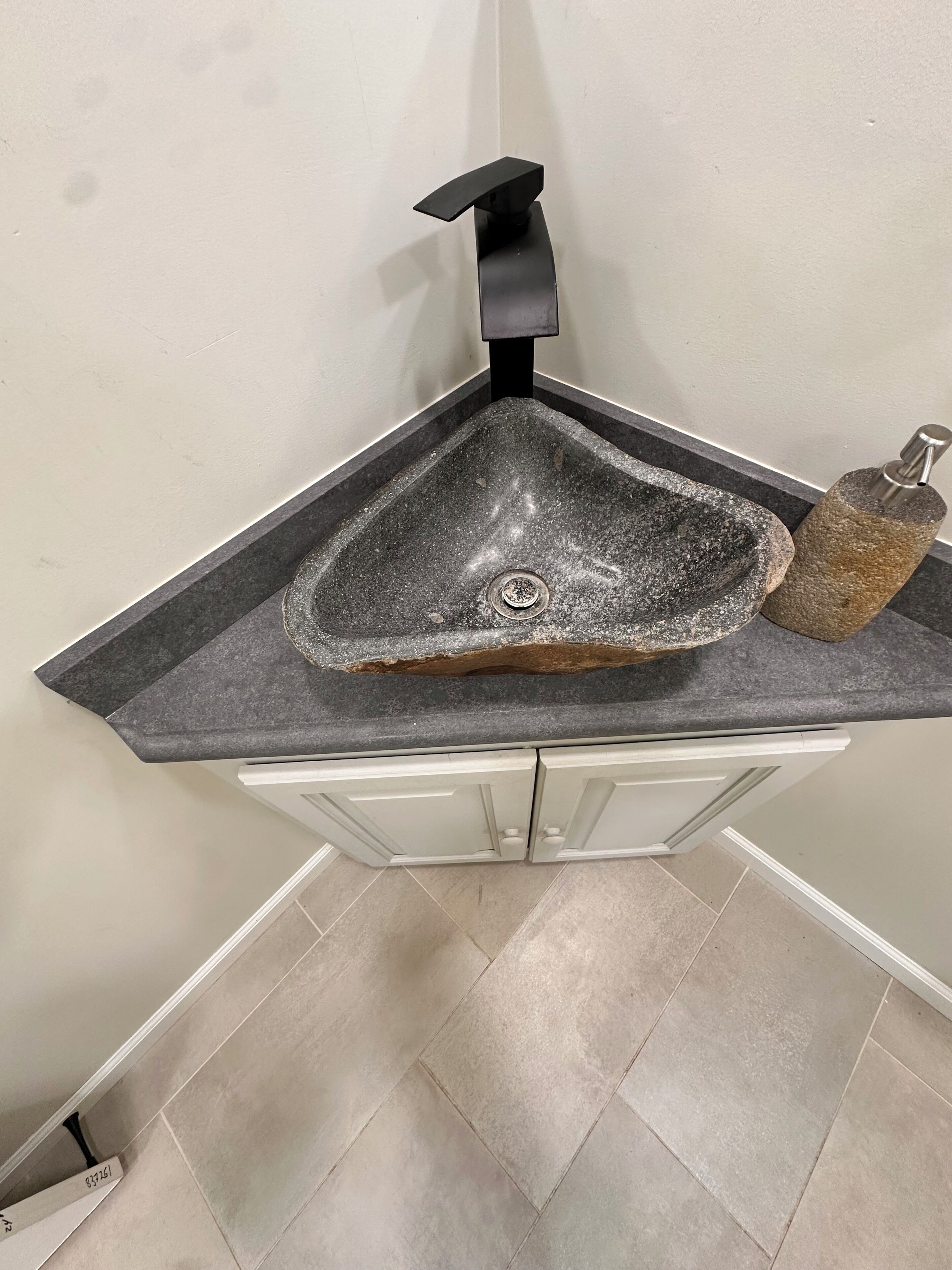 Un évier d’angle au design moderne, un robinet et un plan de travail qui ressemble à de la pierre.