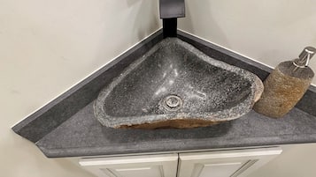 Un évier d’angle au design moderne, un robinet et un plan de travail qui ressemble à de la pierre.