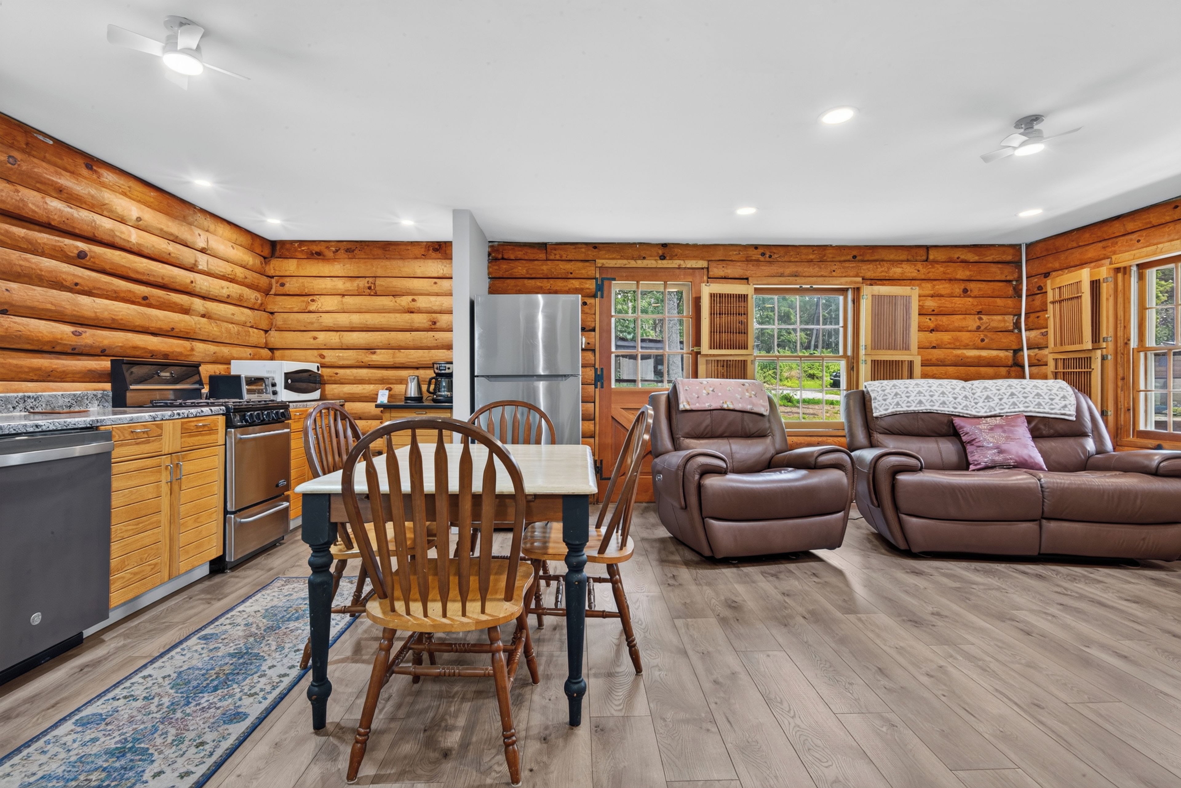 A log cabin interior with a kitchen, dining area, and a seating area with a fireplace.