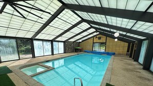 Una piscina interior con techo de cristal, paredes de piedra y vistas al exterior.