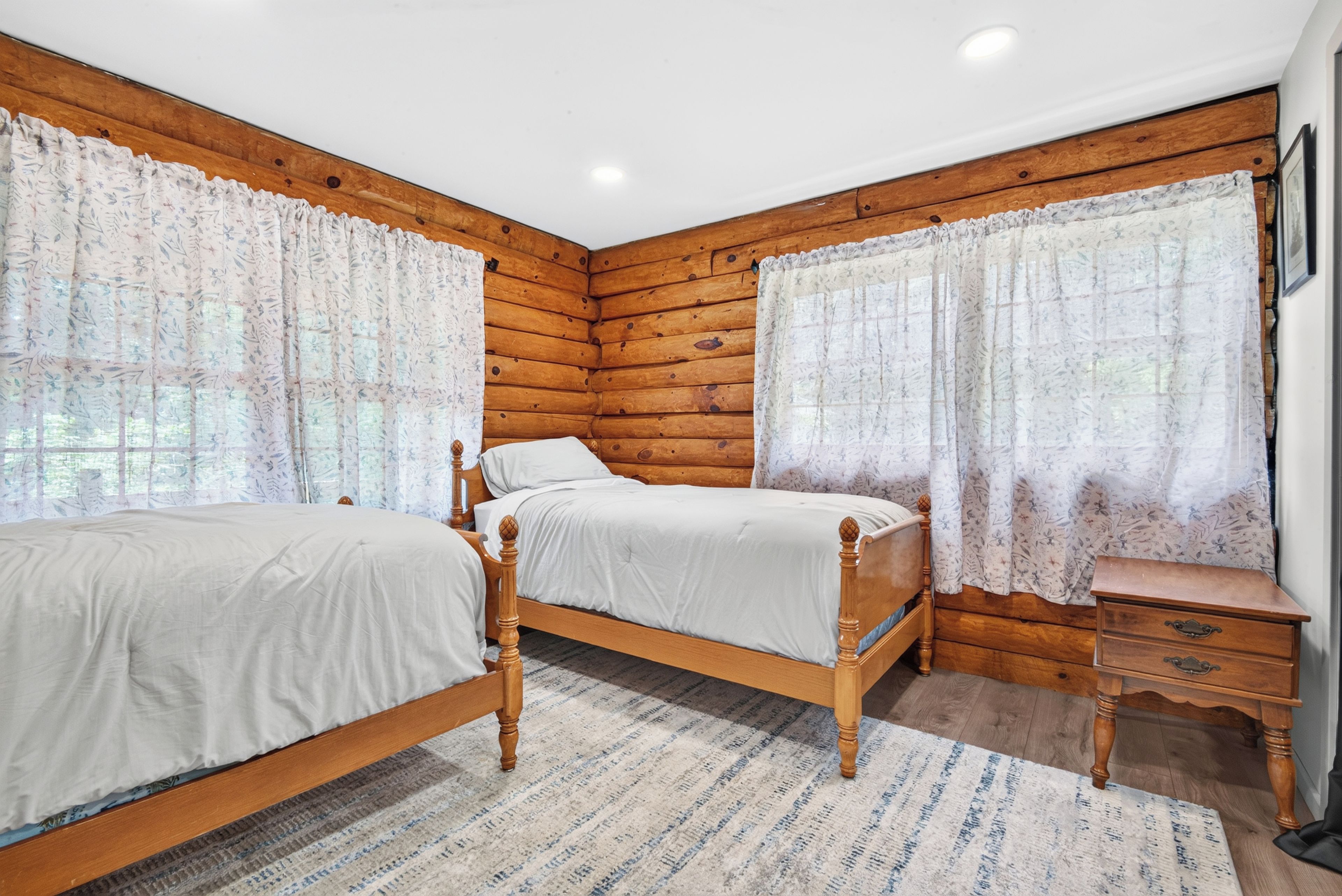 A bedroom with two wooden beds, a wooden nightstand, and a window with curtains.