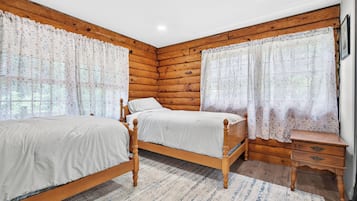 A bedroom with two wooden beds, a wooden nightstand, and a window with curtains.