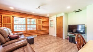 Interior de una cabaña de madera con un sofá de cuero, un televisor y una zona de comedor.