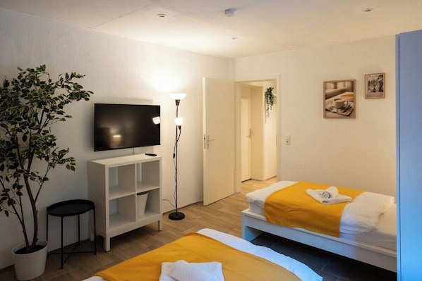 Una habitación de hotel con cama, televisión, planta y estante.