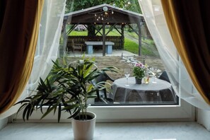 A view through a window with a table set for two, a potted plant, and a gazebo in the background. - Coal Street by Loftigo - House with a Large Garden (Übach-Palenberg)