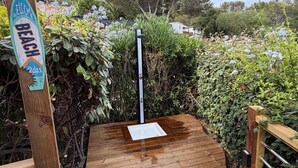 Une terrasse en bois ornée d’une pancarte indiquant « Bienvenue, plage et détente », entourée d’une végétation luxuriante et sous un ciel dégagé.