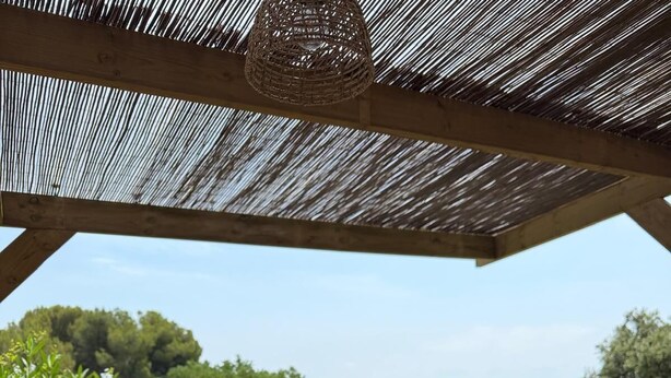 Un espace de restauration en plein air avec une table dressée pour deux personnes, comprenant une assiette de nourriture, une bouteille d’eau et une baguette.