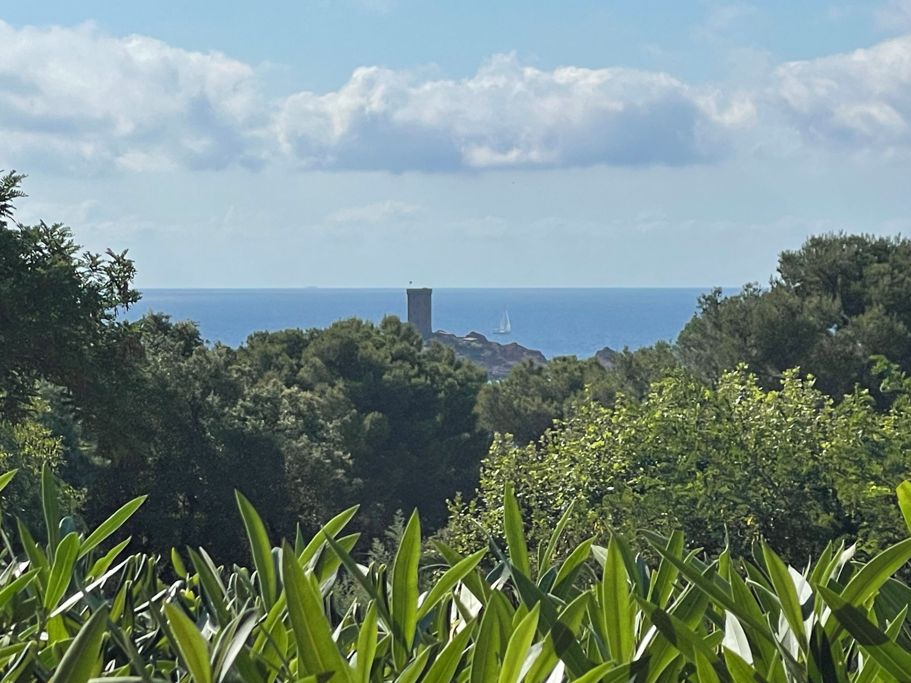 Eine Küstenlandschaft mit üppiger Vegetation, einem entfernten Segelboot und einem turmartigen Bau.