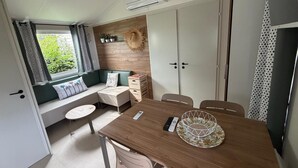 Un espace de vie compact comprenant une table à manger en bois, un canapé intégré avec des coussins, une petite table ronde et un meuble de rangement.