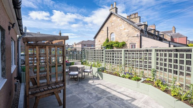 Eine Terrasse mit einer Holz-Pergola, Sitzgelegenheiten im Freien und einem Blumenbeet mit Pflanzen.