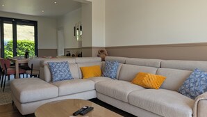 A living room with a sectional sofa, a coffee table, and a dining area with chairs. - House for 8 people • Panoramic View of Lac du Causse • Rated ⭐⭐⭐⭐ • Air-conditioned (Lissac-sur-Couze)