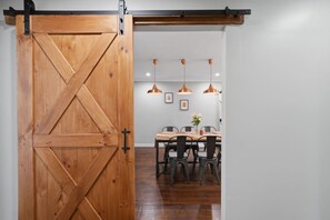 Puerta de madera estilo granero que da a un comedor con una mesa, sillas e iluminación colgante.