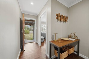 Un pasillo con piso de madera, una puerta que da al exterior, una lámpara de pared y una pequeña mesa con cestas debajo.