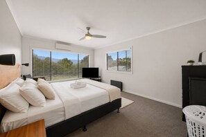 Ein Schlafzimmer mit einem Bett, einem Deckenventilator, einem Fernseher, einem Kamin und Blick durch die Fenster.
