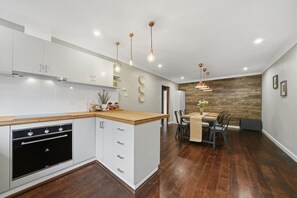 Une cuisine moderne avec des meubles blancs, un plan de travail en bois et un four encastré. On y trouve également un coin repas avec une table et des chaises en bois.