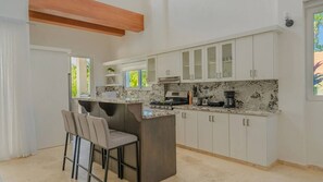 A modern kitchen with white cabinets, a marble countertop, and a bar area with chairs. - Luxe Villa • Gated Community • Caribbean & Sun (Sosúa)