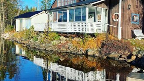 Un chalet au bord du lac doté d’une véranda fermée par des baies vitrées, d’une terrasse en bois et d’un quai.