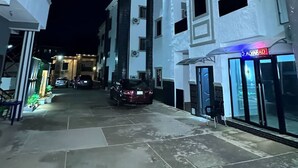 Una calle estrecha flanqueada por edificios, con un coche estacionado y una tienda con letreros iluminados.