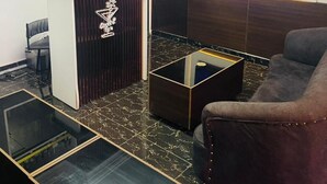 Una sala moderna con un separador de madera oscura, un televisor de pantalla plana, una mesa de centro de vidrio y un sillón de cuero.