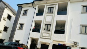 Un edificio de varios pisos con fachada plana, un coche estacionado al frente y un cartel con la palabra 'WELCOME' sobre la entrada.