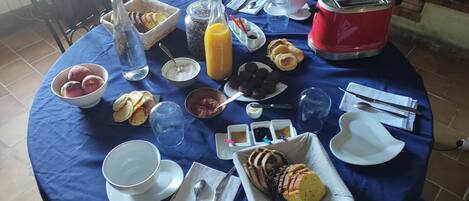 Une table ronde recouverte d’une nappe bleue, avec divers aliments, un grille-pain rouge et une bouteille de jus d’orange.