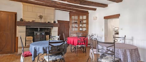 A rustic dining area with exposed wooden beams, a fireplace, and a tiled floor.