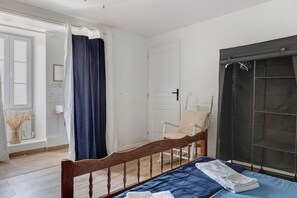 A bedroom with a wooden bed, a chair, a wardrobe, and a window with a curtain.