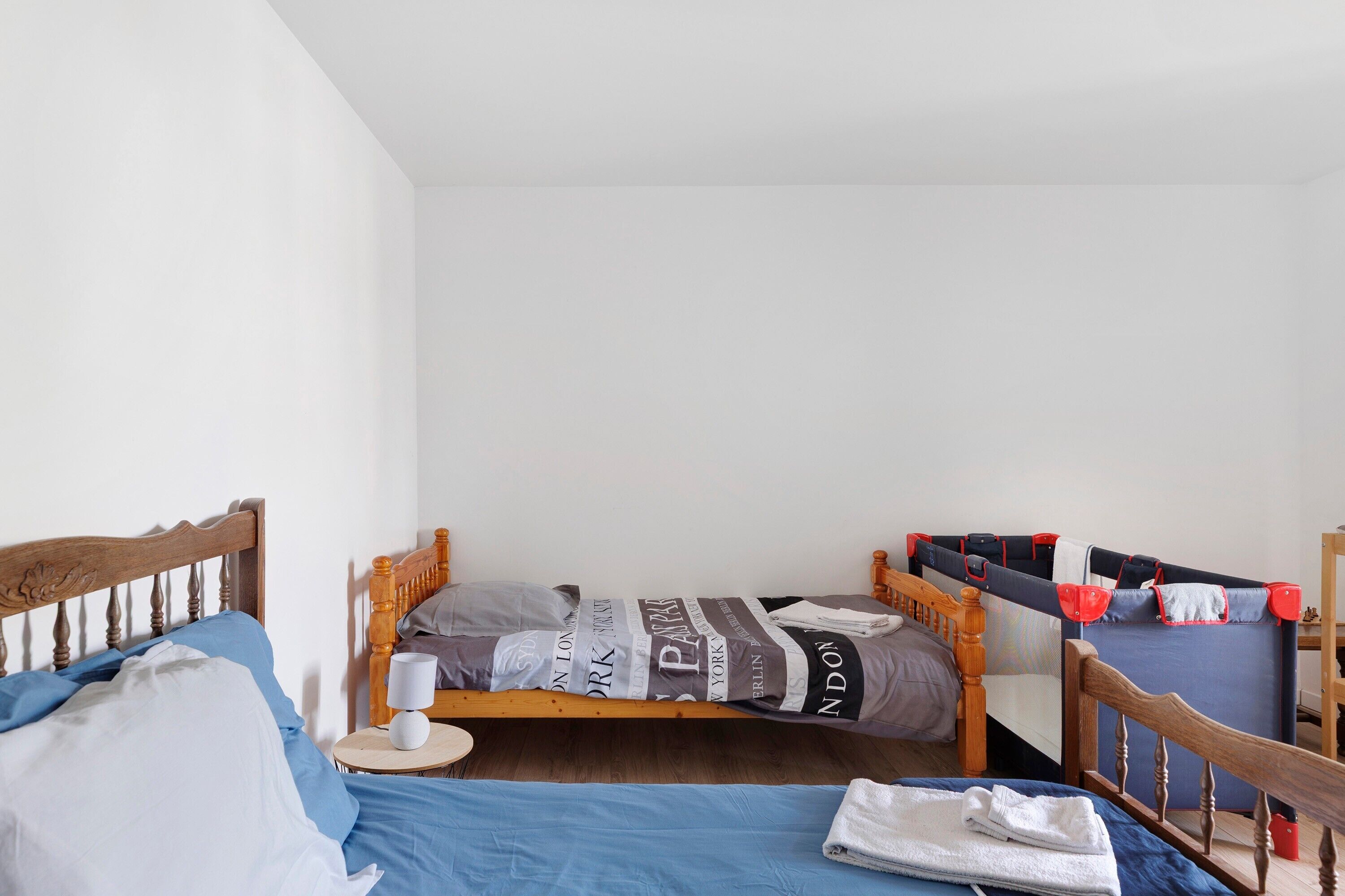 A single bed with a wooden headboard, a bedside table with a lamp, and a blue bedspread.