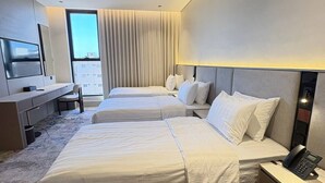 Quarto de hotel com duas camas, uma escrivaninha, uma cadeira, uma televisão e uma janela com cortinas.