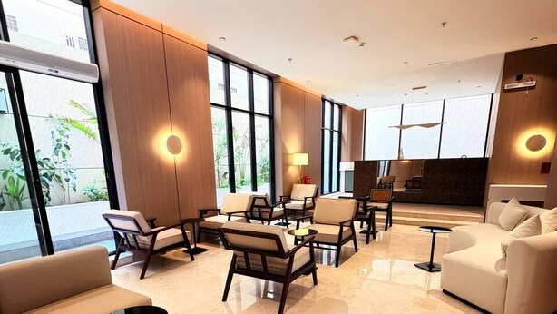 Um saguão de hotel moderno com área de estar, grandes janelas e vista para o verde lá fora.