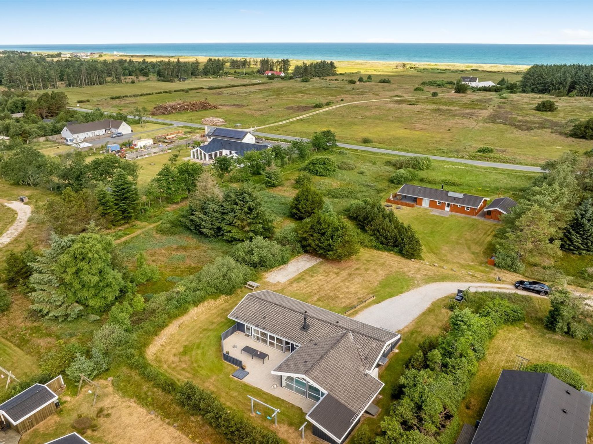 An aerial view of a residential area with multiple houses, a large open field, and a body of water in the background.
