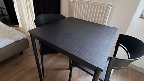 A room with a dark wooden table, two black chairs, a white radiator, and a window with curtains. - Beautiful 1-bedroom apartment in fantastic Poznań location (Poznań)