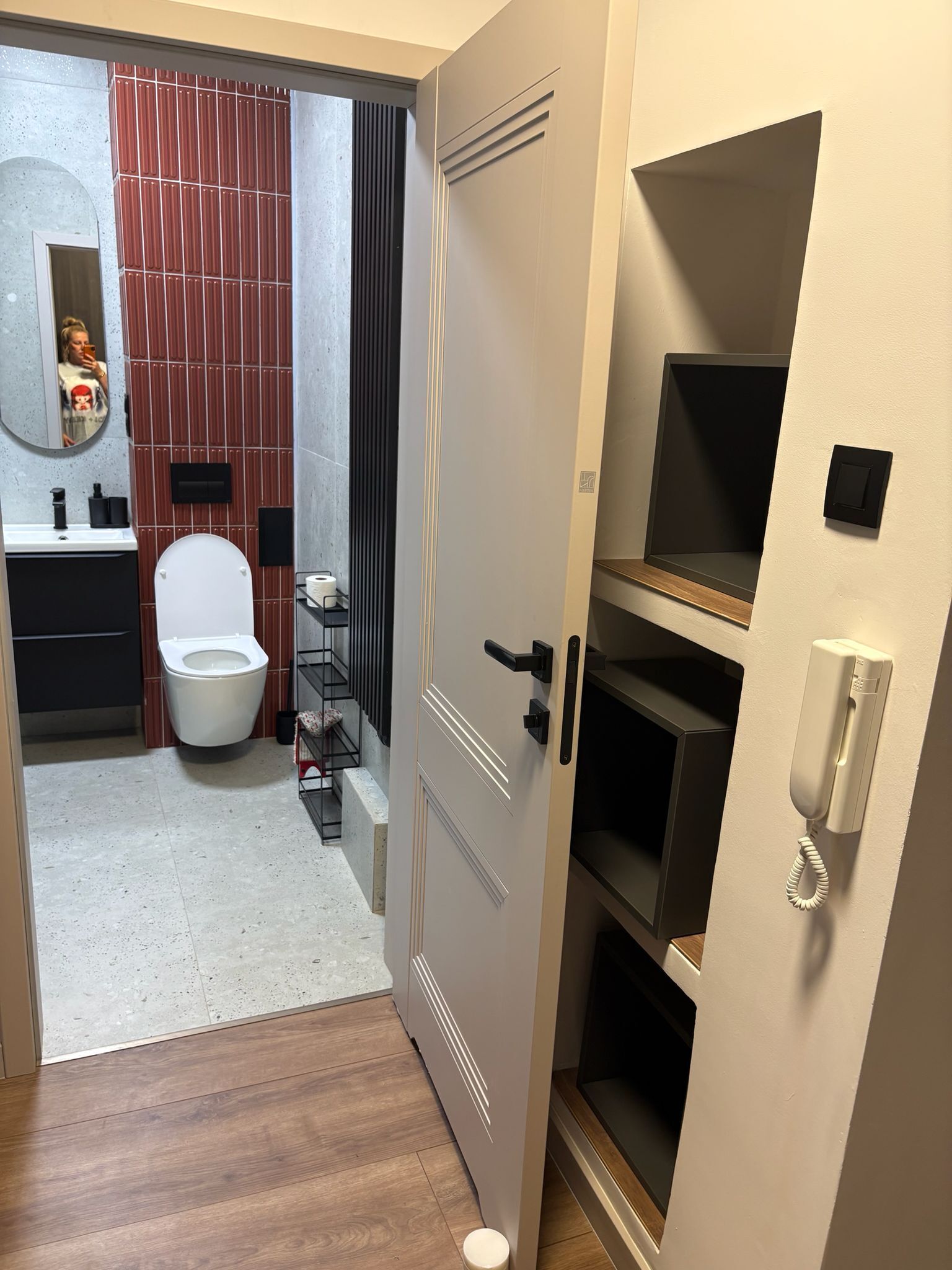 A modern bathroom with a toilet, sink, mirror, and a built-in shelf.
