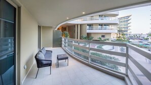 Een balkon met een bank en tafel, een balustrade, en uitzicht op een modern gebouw en straat.