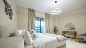 Een moderne slaapkamer met een groot bed, een nachtkastje, een spiegel, een plant en een raam met gordijnen.