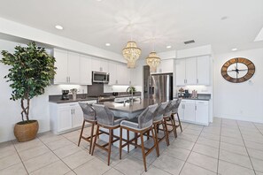 A modern kitchen with white cabinets, a central island with bar stools, stainless steel appliances, and decorative lighting. - Lakefront Indio Luxury Tulum Vacation Home~Pool~Views. (Indio)