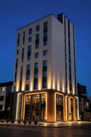 Un hotel de varios pisos con un diseño moderno, que destaca por una entrada con columnas iluminadas y fachada de vidrio.