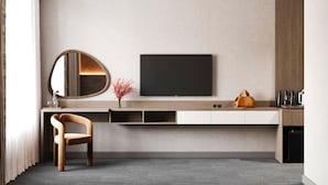 Una habitación de hotel moderna con un televisor de pantalla plana montado en la pared, una silla de madera, una mesita con un florero y un sofá.
