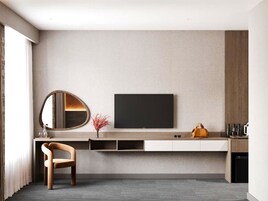 Una habitación de hotel moderna con un televisor de pantalla plana montado en la pared, una silla de madera, una mesita con un florero y un sofá.