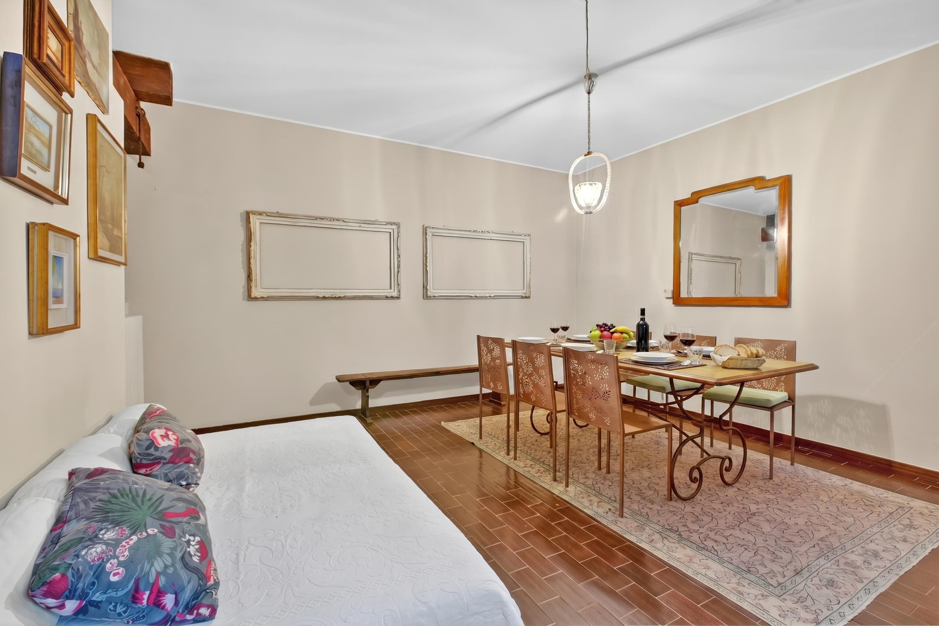 A bedroom with a bed, a dining table with chairs, a mirror, and framed pictures on the wall.