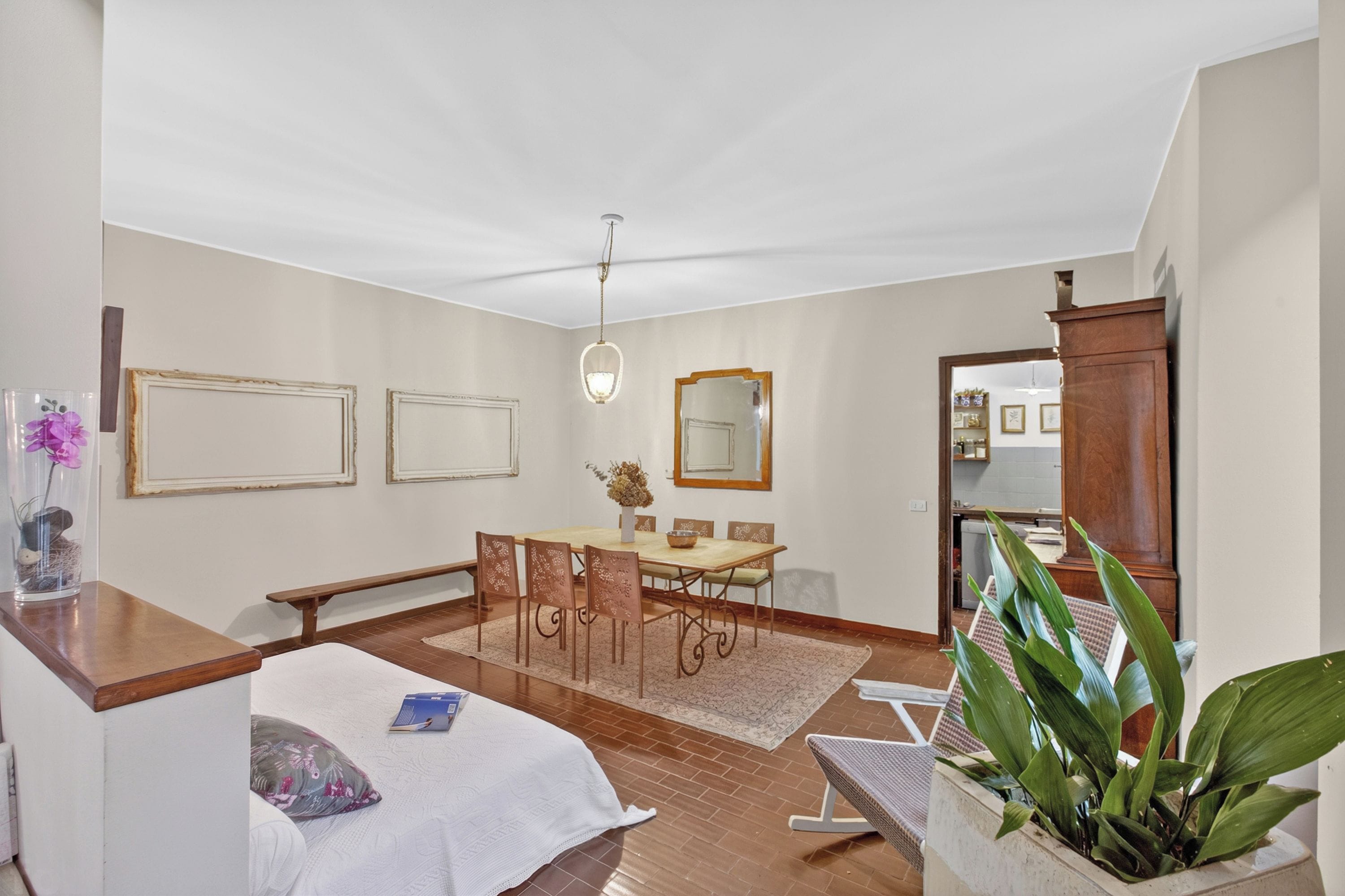 A hotel room with a bed, a desk, a dining table with chairs, a mirror, and a potted plant.