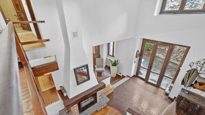 Een meerlaags interieur met een open haard, houten vloeren en een uitzicht door glazen deuren.
