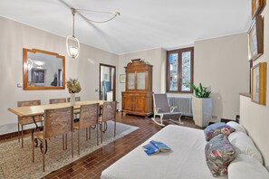 Ein Zimmer mit einem Bett, einem Esstisch mit Stühlen, einem Holzschrank, einem Heizkörper und einem Fenster.
