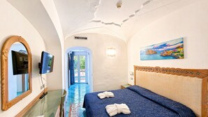Habitación de hotel con una cama, televisor, espejo y un cuadro en la pared.