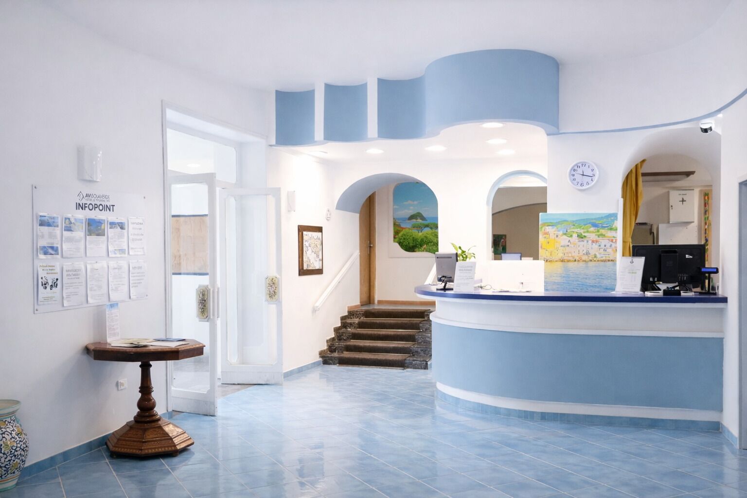 Zona de recepción de hotel con un mostrador curvo, una escalera y un reloj en la pared.