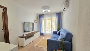 Een moderne woonkamer met een flatscreen televisie, een blauwe bank, een houten salontafel en een kamerplant.